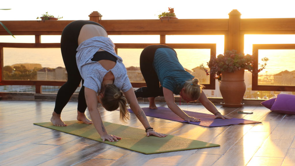Two women are practicing yoga on the terrace of Azul Guesthouse in Morocco, enjoying the sun and a relaxed atmosphere.
