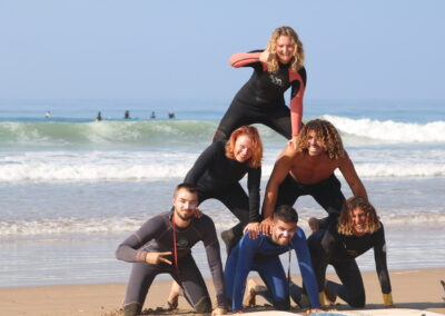 Group of smiling surfers and yogis on the beach after a surf session at Crocro Beach, Morocco