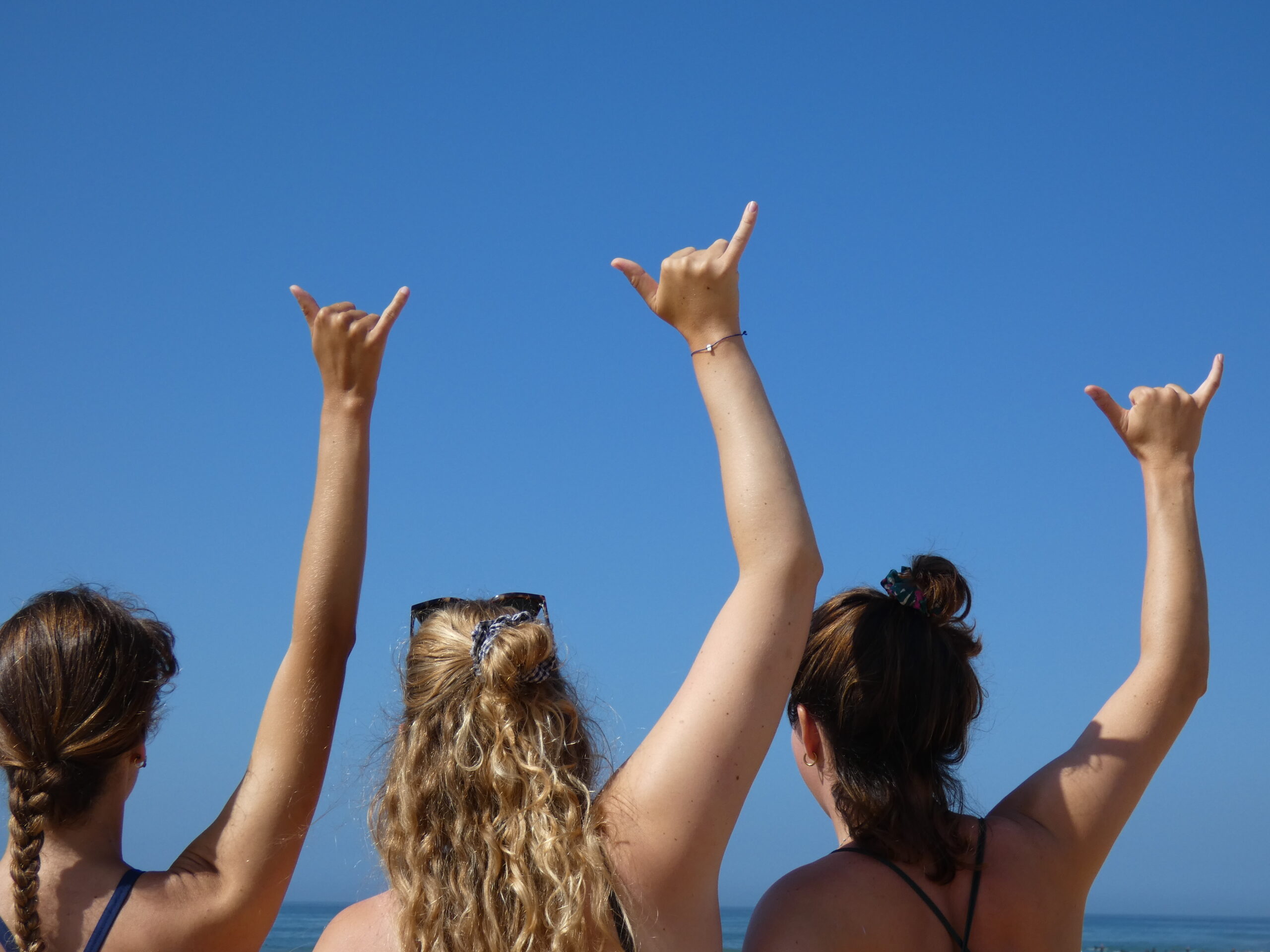 Three girls on the beach in Morocco doing the shaka sign, smiling and enjoying the sun