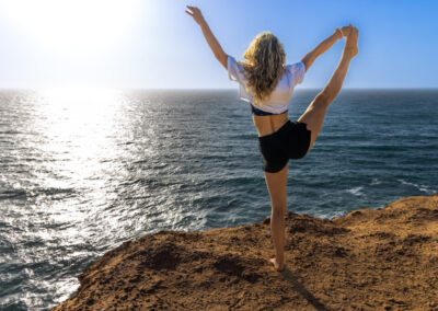 A woman performing a yoga pose on a golden sandy beach in Timlalin, with the ocean in the background and the setting sun.