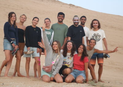 A group of surfers from Azul Guesthouse posing together in the Tamri dunes after an adventurous sand-surfing session at sunset.
